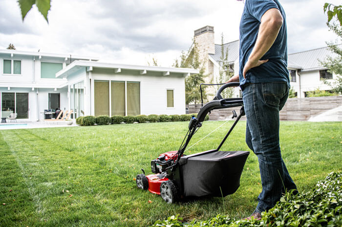 Man with one hand on his hip and the other on his Toro lawnmower in his front yard