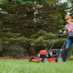 Woman in sunglasses using Toro Recycler in yard surrounded by trees