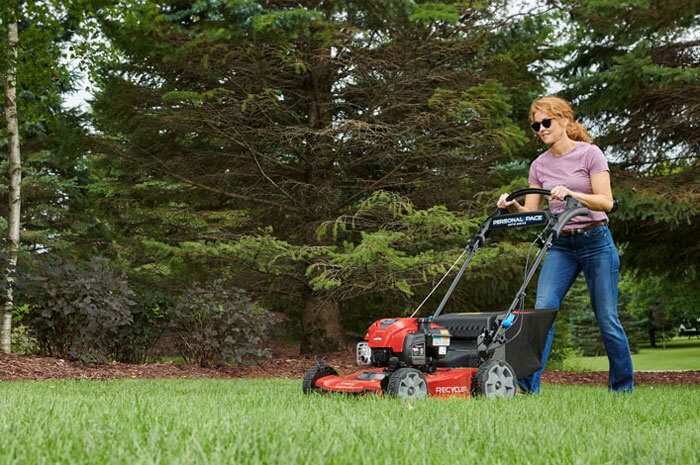 Woman in sunglasses using Toro Recycler in yard surrounded by trees