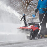 Snowblower on sidewalk blowing snow towards the street