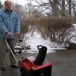 Man standing in driveway with A Toro snowthrower and snow in the background