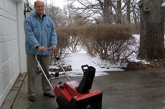 Man standing in driveway with A Toro snowthrower and snow in the background