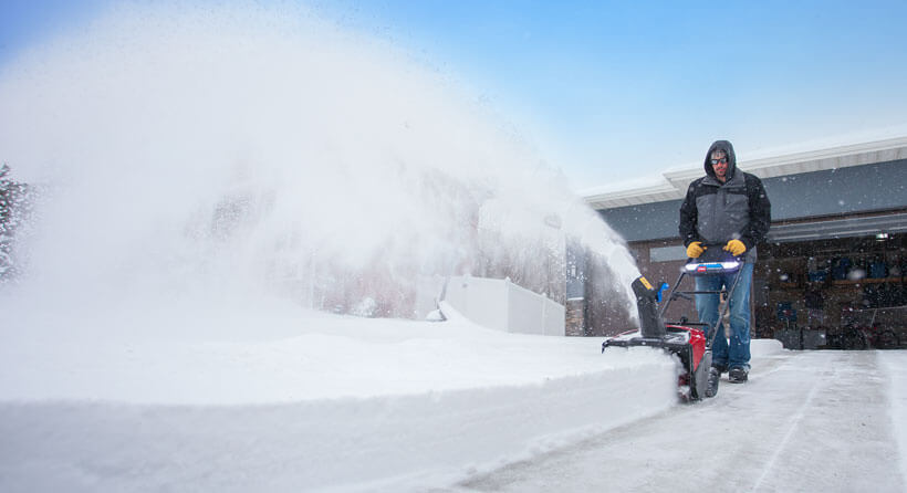 Man using snowblower to clear driveway of fresh snow