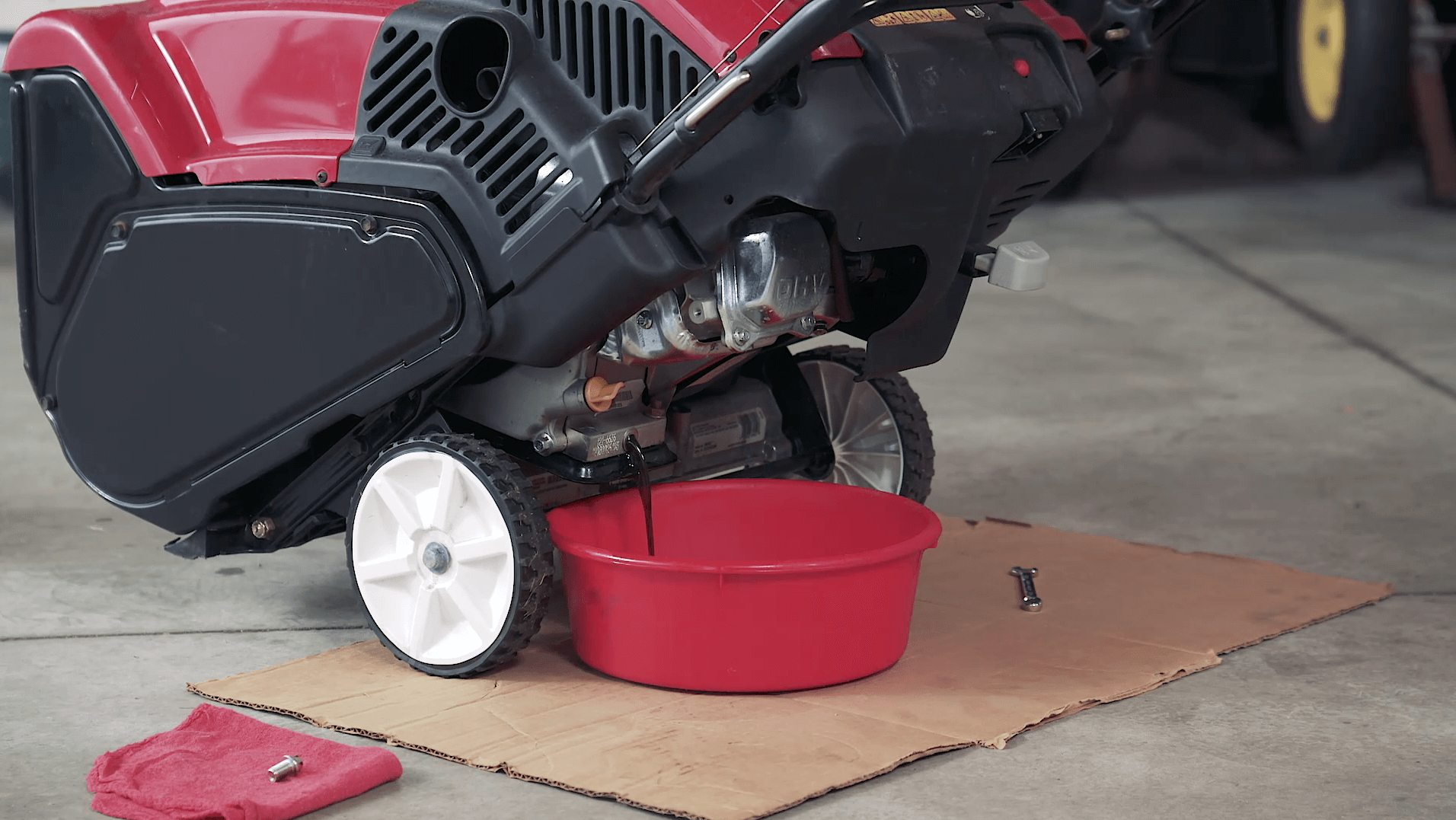 Draining oil from Toro engine into red bucket in garage