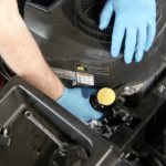 Gloved hands changing lawnmower oil filter
