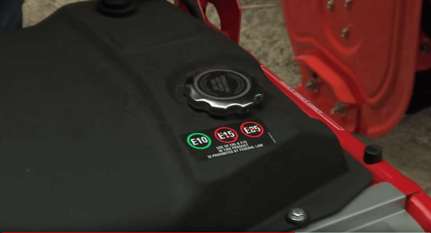 Close up of black fuel tank on lawnmower featuring three types of fuel; E10, E15, E85 with a green circle around E10 and a red circle around E15 and E85 with a warning label stating "Use of E85 & E15 in this product is prohibited by federal law".