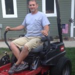 Man in gray shirt sitting on riding mower smiling for photo