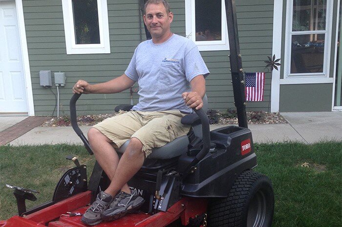 Man in gray shirt sitting on riding mower smiling for photo