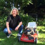 Man kneeling in grass next to Toro Recycler lawnmower