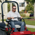 Man using Toro riding lawnmower in the front yard of a suburban home