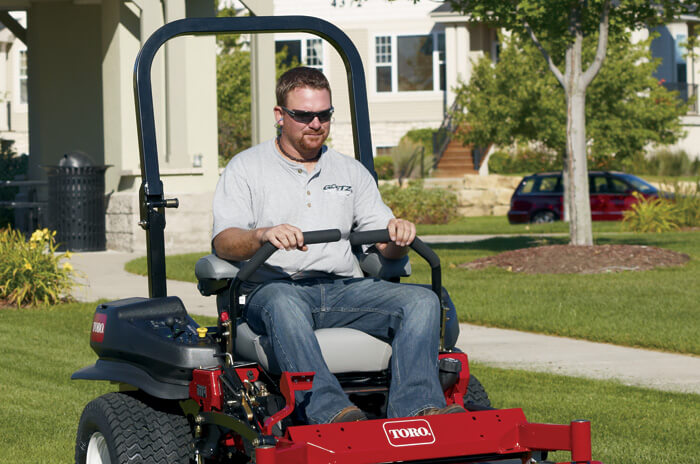 Man using Toro riding lawnmower in the front yard of a suburban home