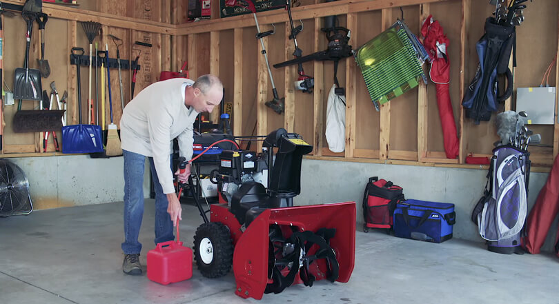 Man in garage fueling Toro product with tube