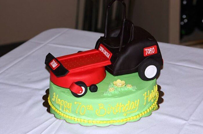 Green cake that says "Happy 70th Birthday" in frosting featuring a Toro lawnmower made of fondant on top