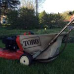Red Toro lawnmower in a green yard with various trees in the background