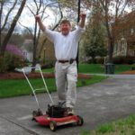 Man with his hands raised above his head, cheering, with Toro lawnmower