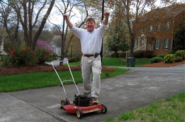 Man with his hands raised above his head, cheering, with Toro lawnmower