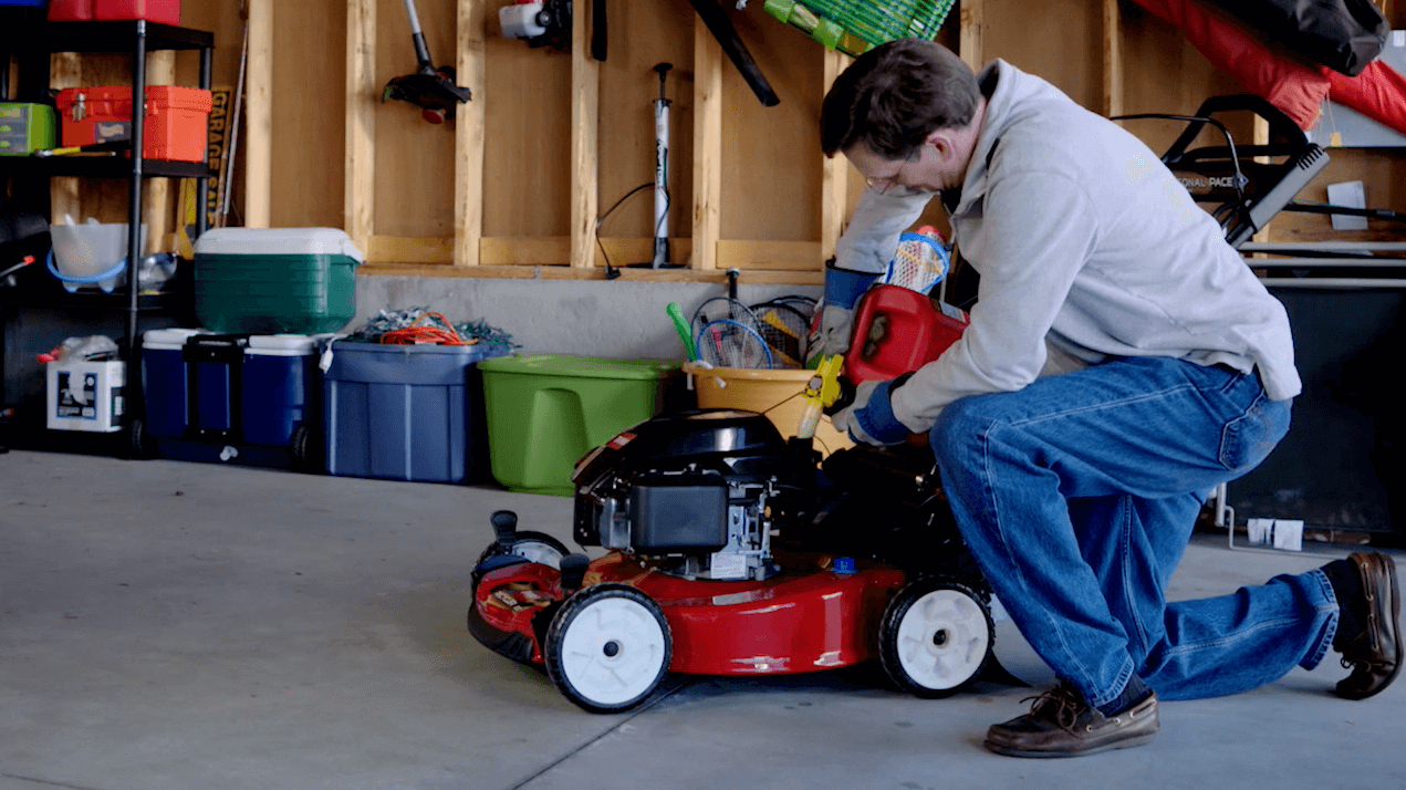 Man in garage adding gas to lawnmower