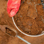 Hand with red glove using tool to sift through soil