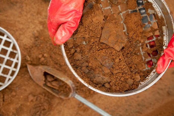 Hand with red glove using tool to sift through soil