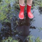 View of person from the leg down, wearing red rain boots standing in a puddle of water