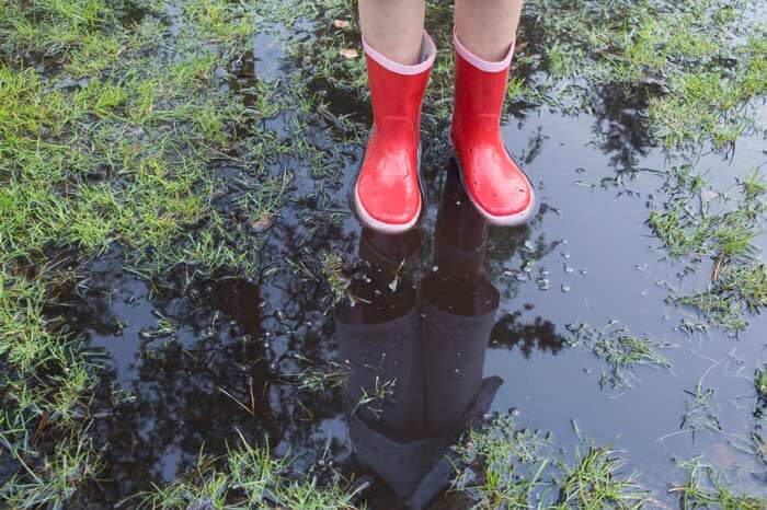 View of person from the leg down, wearing red rain boots standing in a puddle of water