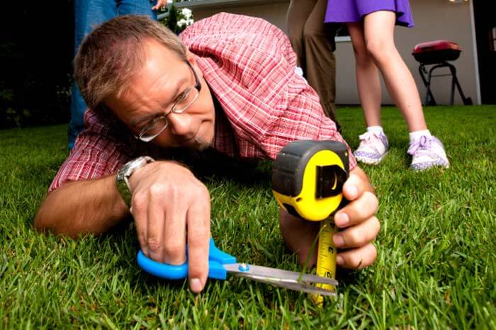 Man with scissors and a tape measurer to cut grass