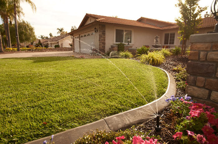 A sprinkler watering green grass outside of a brown home