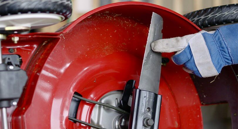 Gloved hand pointing at blade of lawnmower