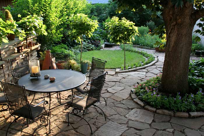 Rock path surrounded by green grass and trees featuring an outdoor patio table and chairs