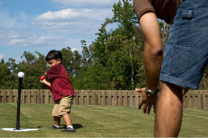 Child about to hit a T Ball with his dad in their backyard