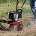 A person using a gas-powered tiller to cultivate soil in a garden.