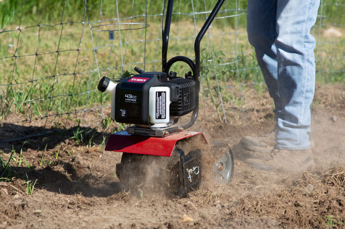 A person using a gas-powered tiller to cultivate soil in a garden.